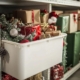 A white storage bin filled with holiday decorations, including wrapped presents and ornaments, on a shelf.